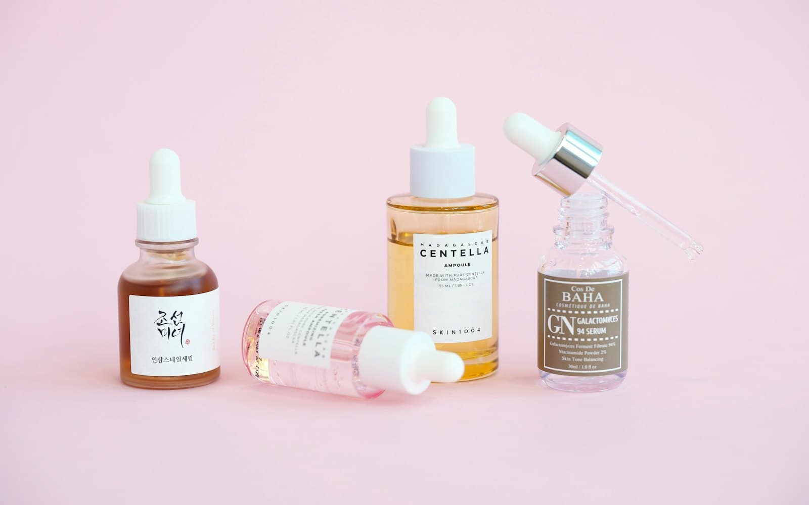 A row of serums and dropper bottles lined up on a pink surface