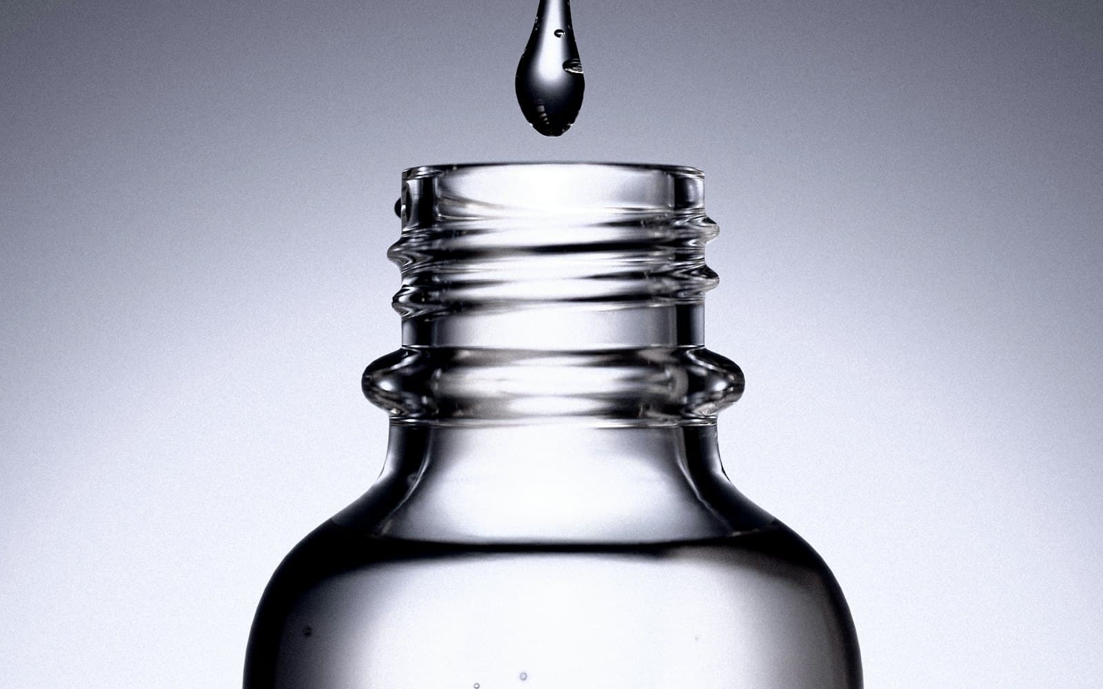 A single drop of serum falling into a glass bottle